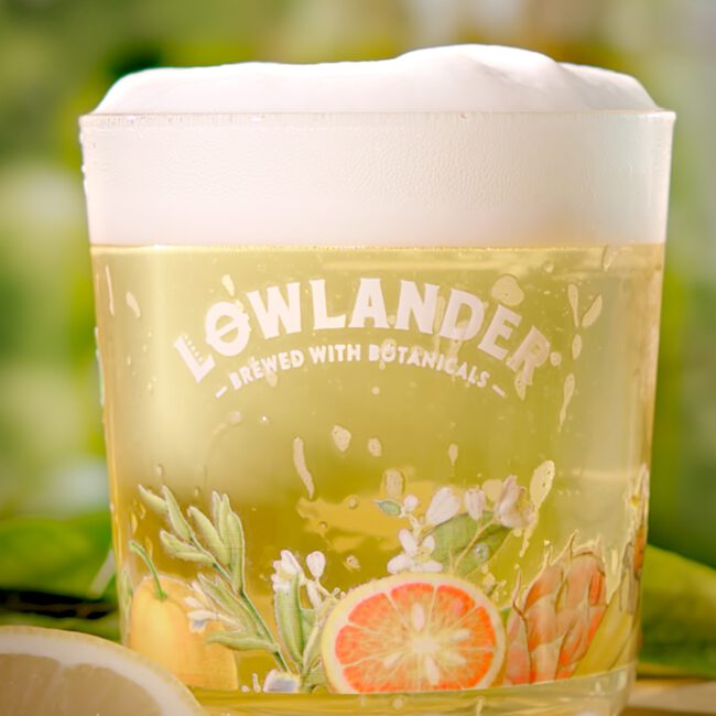 Lowlander packshot bierglas met bier en schuimkraag, achtergrond groene kas.